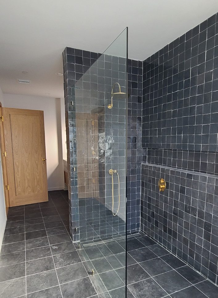 Dark zellige-tiled shower with brass fixtures